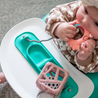 Baby chewing on Busy Baby Crab Teether attached to Busy Baby Mini Mat silicone mat on small tray