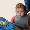 Baby at table with Blue Busy Baby Mat silicone mat and wearing Pewter Busy Baby Stop Drop Bib