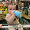 Baby in shopping cart at grocery store with bottle attached to Tan Busy Baby Bottle Bungee wrapped around cart handlebar