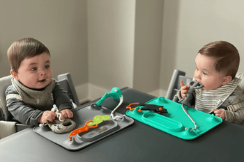 twins with busy baby silicone suction placemat on table snacking and playing