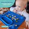 A baby sitting at a restaurant table sitting in a highchair eating food from a busy baby original placemat