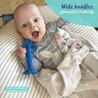 A baby laying in a baby pillow holding the Busy Baby 2-in-1 Teether & Training Spoon with a big smile