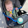 Baby sitting in a stroller with the busy baby bottle bungee and busy baby boy bungee strapped around either side of the stroller handle with a bottle and toy attached