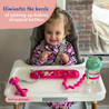 A baby sitting at a highchair with the Busy Baby Mini Mat on the surface and Bottle Bungee with cup attached to mat. The Busy Baby Teething Spoon is also attached to the mat with a Tether.