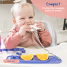 A baby sitting at a highchair teething on a Teether attached to the Busy Baby mini mat that is on the surface of the highchair with two orange slices in the mini mat tray.