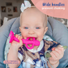 A baby sitting in a highchair holding the Busy Baby 2-in-1 Teether & Training Spoon with a big smile