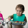 Baby eating off of Busy Baby Mat silicone mat wearing and using Spearmint Busy Baby Stop Drop Travel Bib+Utensils