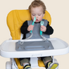 Baby sitting in highchair holding Busy Baby Utensils attached to Busy Baby Mat silicone mat