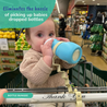 Baby sitting in a grocery store shopping cart with busy baby bottle bungee attached to cart handle and bottle attached to the bottle bungee while baby drinks