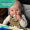 A baby sitting at a compact highchair with the busy baby toy bungee attached to the mini mat chewing on the busy baby sloth teether